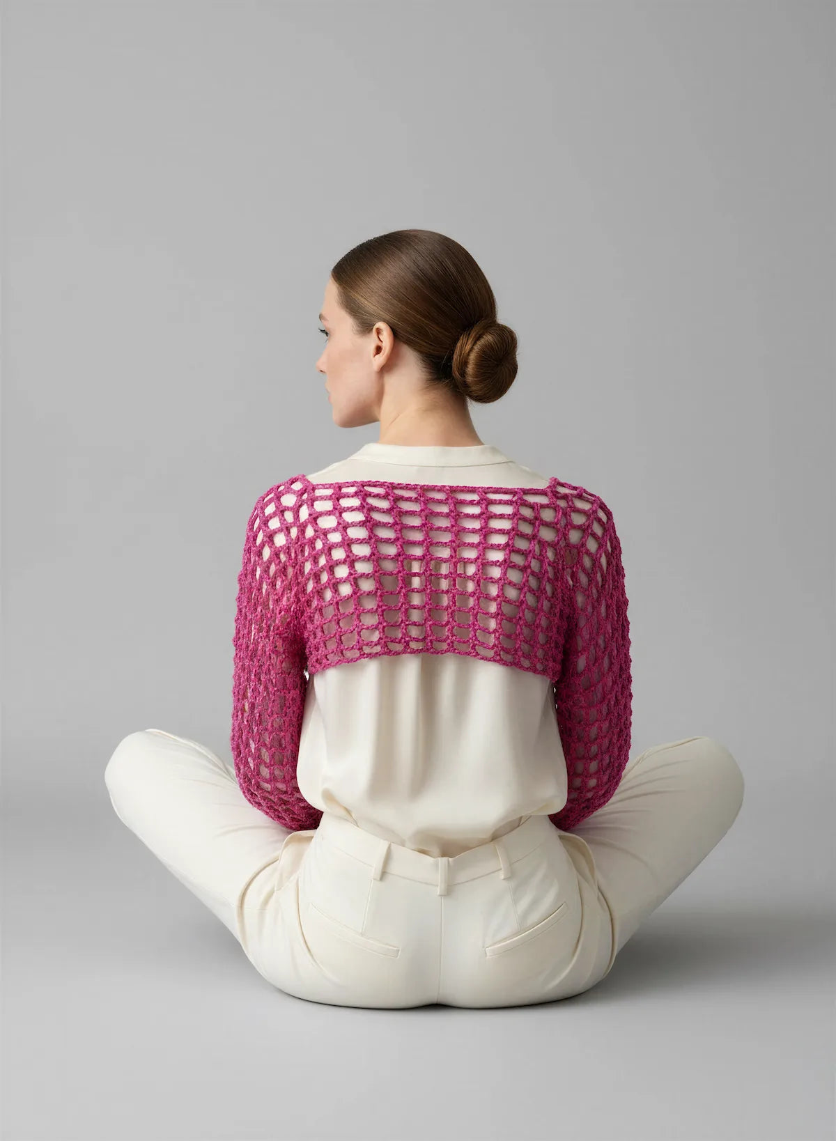 Crop Top Fuschiamo – vue de dos assise en tailleur – crop top crochet fait main fuchsia résille grande maille encolure dos bateau chignon élégant – Cachalabibi