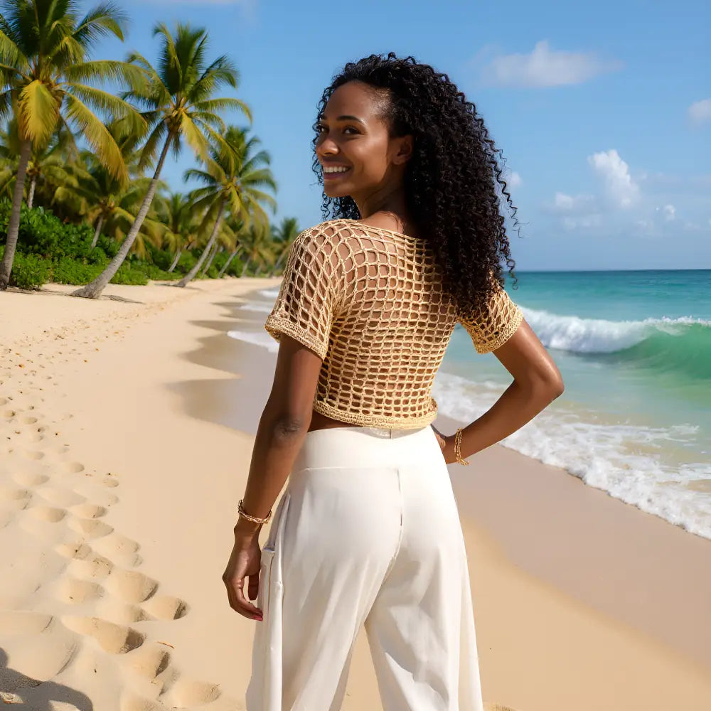 Haut au crochet fait main Kobieta de Cachalabibi - beige foncé - vue de dos d'une jeune femme en pantalon blanc à la plage