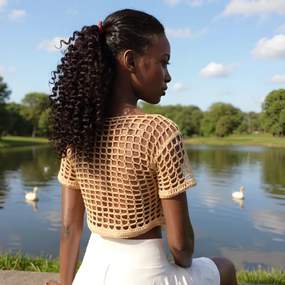 Haut au crochet fait main Kobieta de Cachalabibi - beige foncé - vue de dos d'une jeune femme aux cheveux noués assise au bord d'un étang