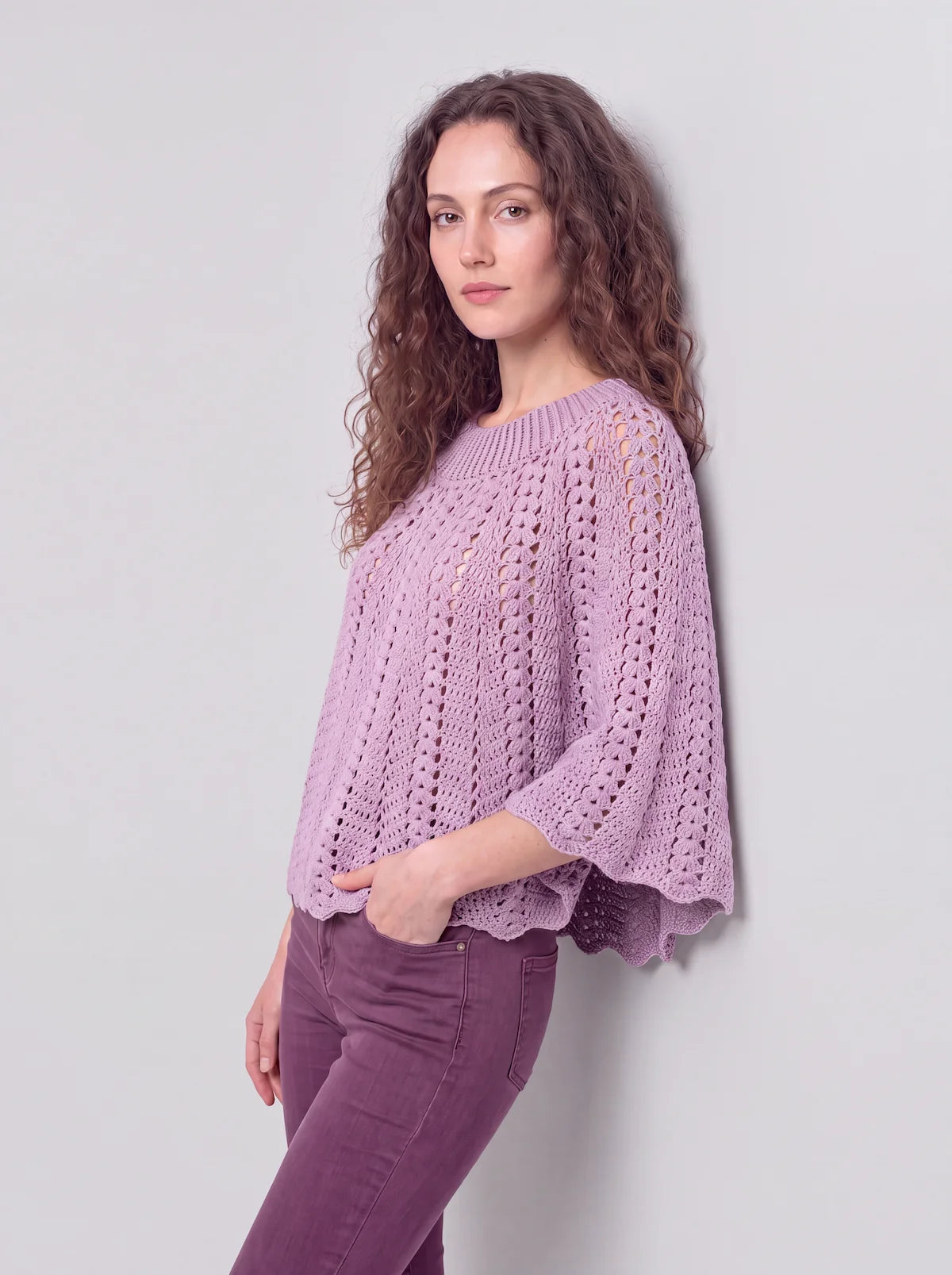 Poncho femme Violyne au crochet lilas, vue adossée à un mur, point éventail et granny squares, manches évasées - cachalabibi