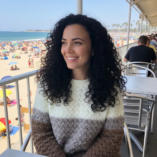 Pull au crochet fait main Passero de Cachalabibi - gris perle et marron - vue de face d'une jeune femme en terrasse près de la plage