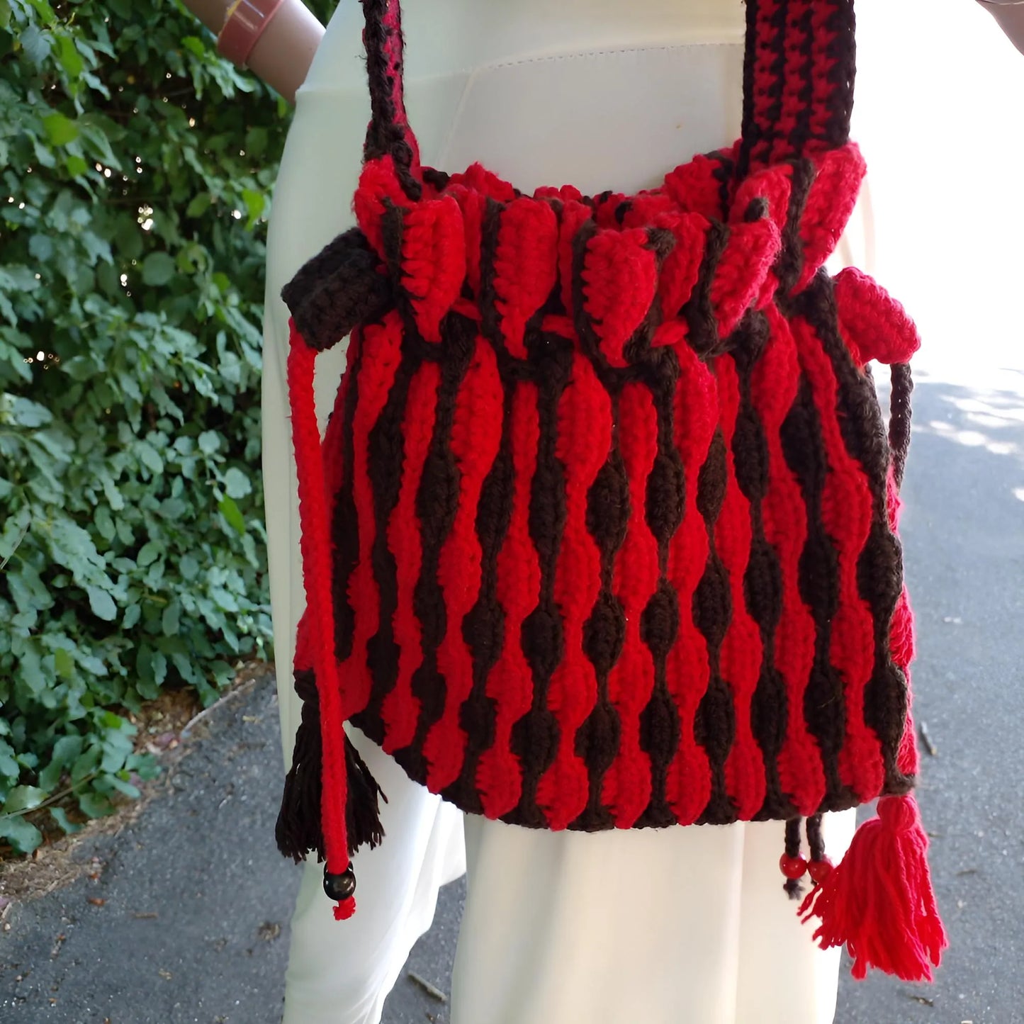 Sac à main au crochet fait main Rossonero de Cachalabibi - rouge et noir - gros plan sur le sac montrant la fermeture à cordon et les pompons décoratifs