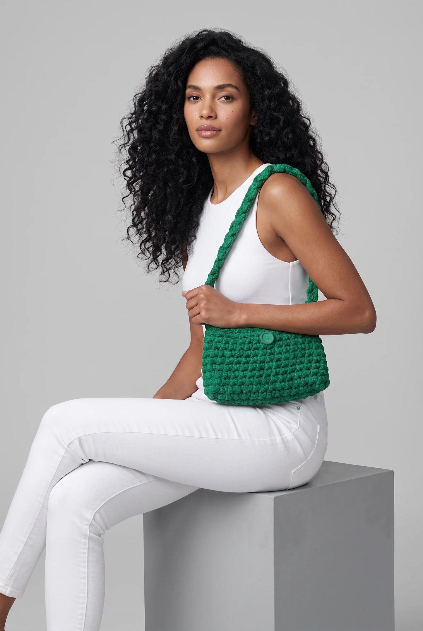 Sac à main au crochet fait main Menta vert de Cachalabibi - assise sur un cube avec pantalon blanc