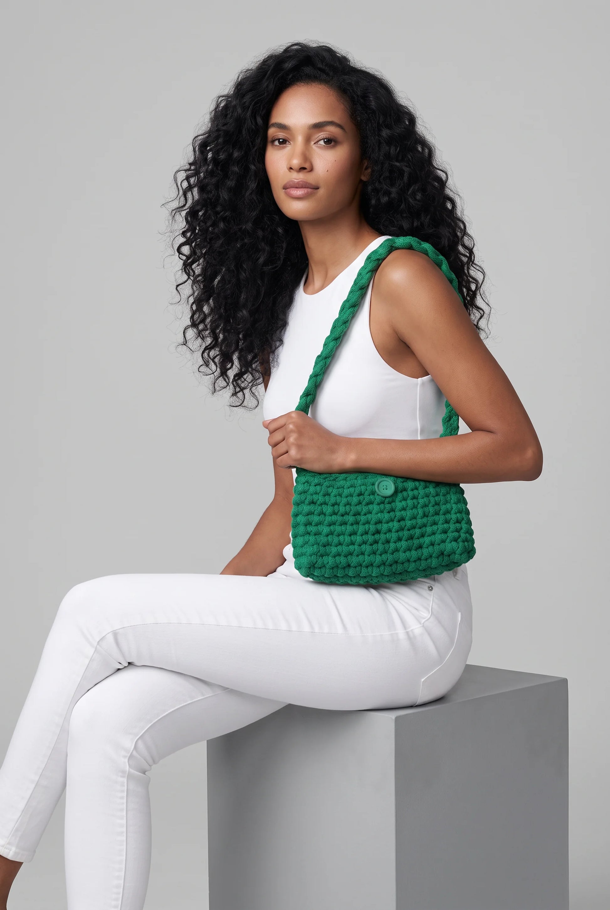 Sac à main au crochet fait main Menta vert de Cachalabibi - assise sur un cube avec pantalon blanc